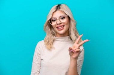 Genç Rus kadın mavi arka planda gözlüklü ve iyi işareti olan izole edilmiş.