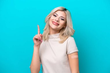 Yara bandı takan genç Rus kadın mavi arka planda izole edilmiş harika bir fikre işaret ediyor.