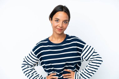 Beyaz arka planda soyutlanmış, kalçasında kollarıyla poz veren ve gülümseyen genç İspanyol kadın.