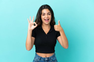 Mavi arka planda izole edilmiş genç beyaz kadın işaret ve baş parmak hareketi gösteriyor.