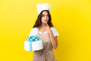 Sarı arka planda izole edilmiş büyük bir pastası olan Kafkasyalı genç aşçı kadın yukarı bakarken şüpheleri vardı.