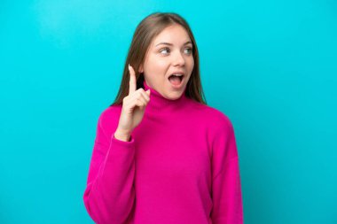 Genç Litvanyalı bir kadın mavi arka planda izole edilmiş bir şekilde parmağını kaldırarak çözümü anlamaya çalışıyor.
