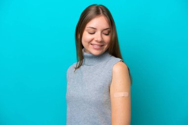 Yara bandı takan Litvanyalı genç bir kadın mavi arka planda mutlu bir ifadeyle izole edilmiş.