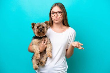 Mavi arka planda köpeği tutan Litvanyalı genç bir kadın omuzlarını kaldırırken şüpheyle hareket ediyor.