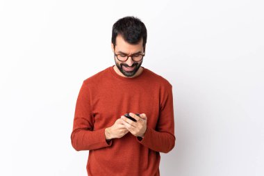 İzole edilmiş beyaz arka planı olan beyaz sakallı, beyaz, yakışıklı bir adam cep telefonuyla mesaj gönderiyor.