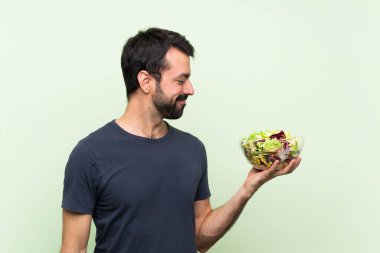 Yeşil duvarın üstünde salatalı yakışıklı bir genç.