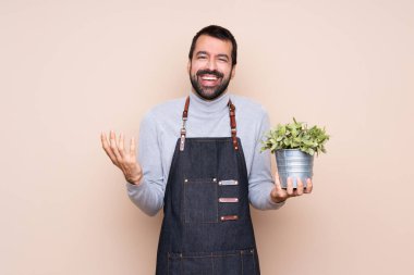 Arka planda bir bitkiyi tutan adam çok fazla gülümsüyor.