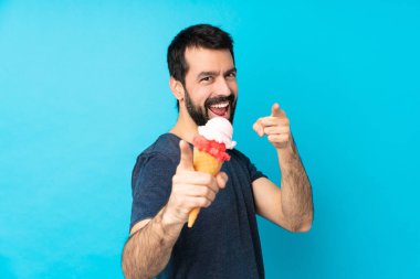 Kornet dondurması ile izole edilmiş mavi arka plan üzerindeki genç adam gülümserken seni işaret ediyor.