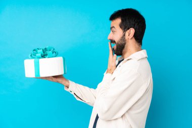 Büyük pastası olan genç ve yakışıklı bir adam izole edilmiş mavi arka planda