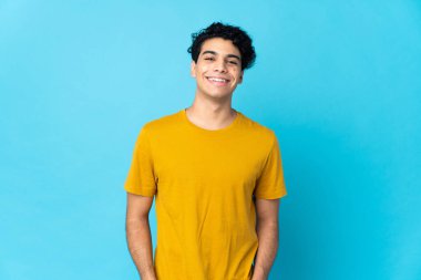 Genç Venezuelalı adam mavi arka planda izole edilmiş gülüyor.