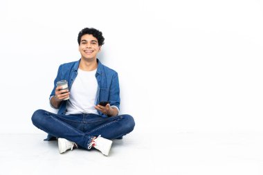 Venezuelalı bir adam kahve alıp götürmek için yerde oturuyor. Bir de cep telefonu.