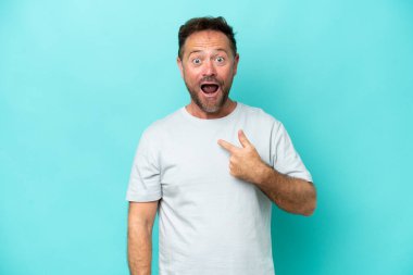 Orta yaşlı beyaz bir adam mavi arka planda izole edilmiş ve yüzünde sürpriz bir ifade var.