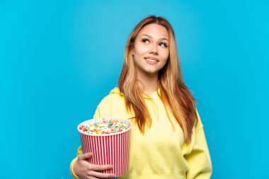 Mavi arka planda patlamış mısırları tutan genç kız yukarı bakarken bir fikir düşünüyor.