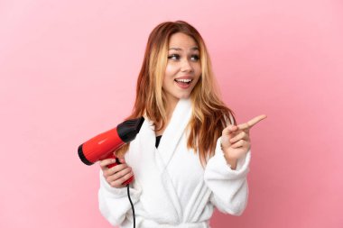 İzole edilmiş pembe arka plan üzerinde saç kurutma makinesi tutan genç sarışın kız çözümü fark etmek için parmağını kaldırıyor.
