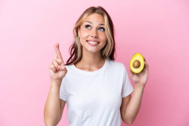 Avokado tutan genç Rus kadın pembe arka planda izole edilmiş, şans diliyor ve en iyisini diliyor.