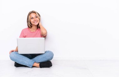 Yerde dizüstü bilgisayarı olan genç bir Rus kız beyaz arka planda izole edilmiş bir şekilde oturuyor.