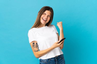 Genç Slovak kadın mavi arka planda izole edilmiş ve telefon zafer pozisyonunda.