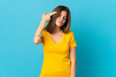 Genç Slovak kadın mavi arka planda izole edilmiş ve intihar jesti yapmada sorun yaşıyor.