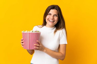 Sarı arka planda izole edilmiş genç Slovak kadın elinde koca bir kova patlamış mısır tutuyor.