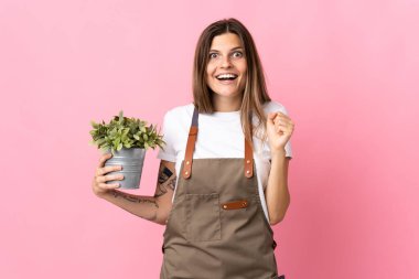 Bahçıvan kadın pembe arka planda bir bitki tutuyor galibiyetini kutluyor.