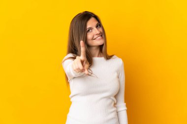 Sarı arka planda izole edilmiş genç Slovak kadın parmağını kaldırıyor ve gösteriyor