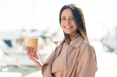 Açık havada elinde kahveyle gezen genç bir kadın.