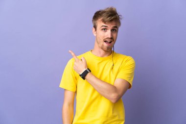 Mor arka planda soyutlanmış yakışıklı sarışın adam şaşırmış ve işaret ediyor.