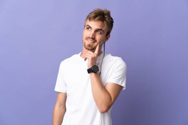 Genç yakışıklı sarışın adam mor arka planda izole edilmiş bir şekilde bakarken bir fikir düşünüyor.
