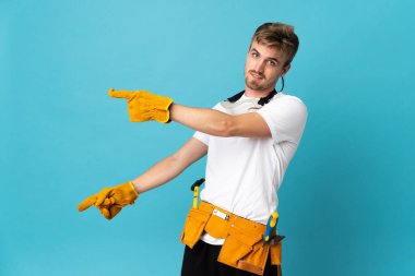 Genç elektrikçi, izole edilmiş duvarın üzerinden parmak göstererek bir ürün sunuyor.