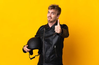 Motosiklet kasklı bir adam sarı arka planda izole edildi. Başparmakları havada çünkü iyi bir şey oldu.