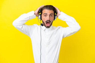 Tele pazarlamacı beyaz adam sarı arka planda izole edilmiş bir kulaklıkla çalışıyor. Sürpriz bir ifadeyle.