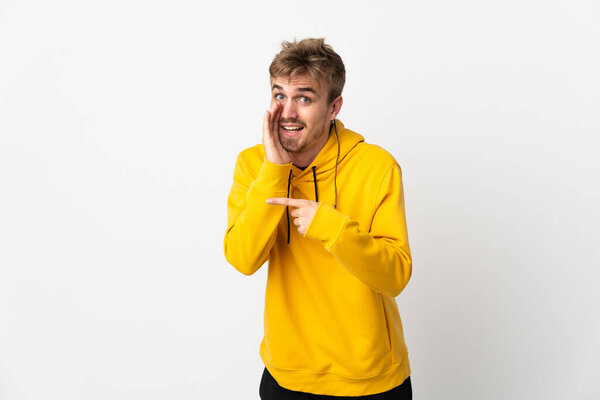 Молодой красивый мужчина изолирован на белом фоне, указывая на сторону, чтобы представить продукт и шепчет что-то