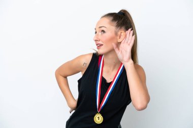 Young caucasian woman with medals isolated on white background listening to something by putting hand on the ear