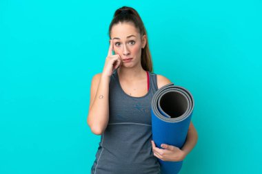 Kafkasyalı genç bir kadın yoga derslerine giderken elinde mavi arka planda bir minder tutarak bir fikir düşünüyor.