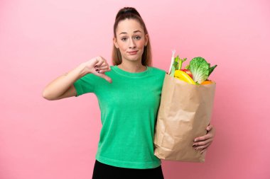 Elinde alışveriş poşeti tutan genç bir kadın olumsuz bir ifadeyle baş parmağını aşağı gösteriyor.