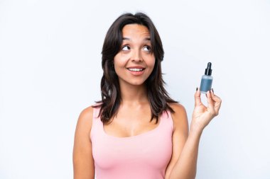 Beyaz arka planda serumu tutan genç İspanyol kadın yukarı bakarken bir fikir düşünüyor.