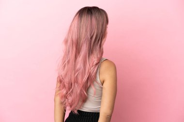 Pembe saçlı melez bir kadın pembe arka planda izole edilmiş ve arkasına bakıyor.