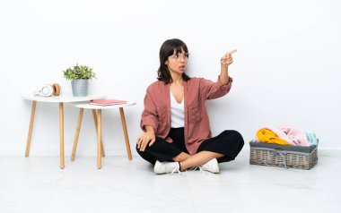 Genç melez kadın, beyaz arka planda soyutlanmış bir şekilde yerde oturmuş kıyafetlerini katlıyor.