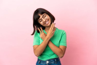 Pembe arka planda izole edilmiş genç melez kadın gülümsüyor ve zafer işareti gösteriyor.