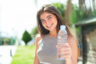 Açık havada elinde bir şişe su olan güzel beyaz bir kadın.