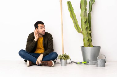 Bahçıvan içeride yerde oturup bir şeyler dinlerken elini kulağına koydu.