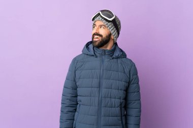 Kar kaykayı gözlüklü kayakçı mor arka planda yukarı bakarken bir fikir düşünüyor.