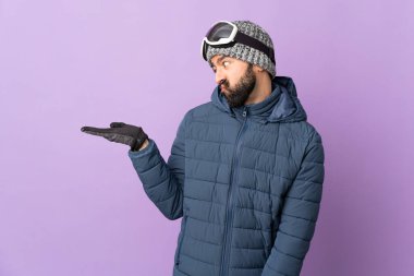 İzole edilmiş mor arkaplan üzerinde snowboard gözlüklü kayakçı. Kopyalama alanını şüpheyle tutuyor.