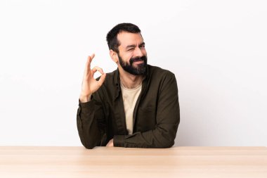 Masada sakallı, beyaz bir adam. Parmaklarıyla 