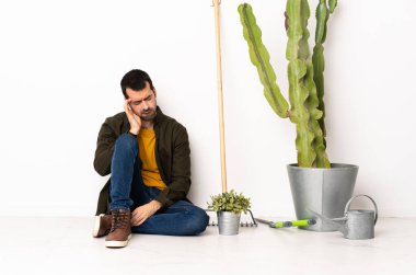 Bahçıvan adam baş ağrısıyla yerde oturuyor.