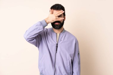 Sakallı, ceketli, soyutlanmış arka planda beyaz bir adam. Gözleri elleriyle kaplıyor ve gülümsüyor.