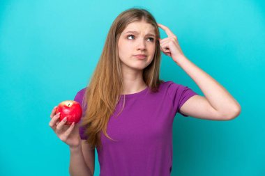 Genç ve güzel bir kız elmayı soyutlanmış mavi arka planda tutarak bir fikir düşünüyor. 