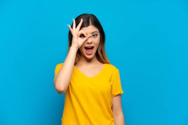 Young Russian girl isolated on blue background showing ok sign with fingers