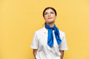 Uçak hostesi sarı arka planda izole edilmiş ve yukarı bakıyor.