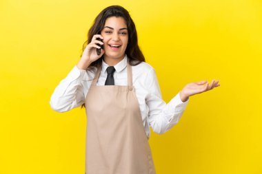 Genç Kafkas lokantası garsonu sarı arka planda izole edilmiş cep telefonuyla sohbet ediyor.